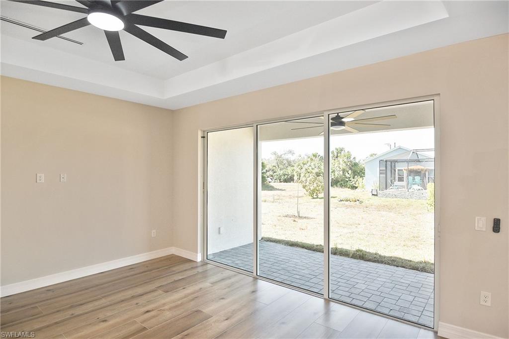 Spacious room featuring wood-finish flooring, a tray ceiling, and a modern ceiling fan with integrated lighting
