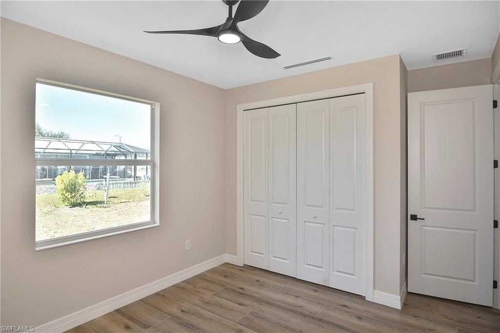 Neutral-toned interior featuring wood-finish flooring, a contemporary ceiling fan, a large window, a bi-fold closet, and a paneled door with matte black hardware