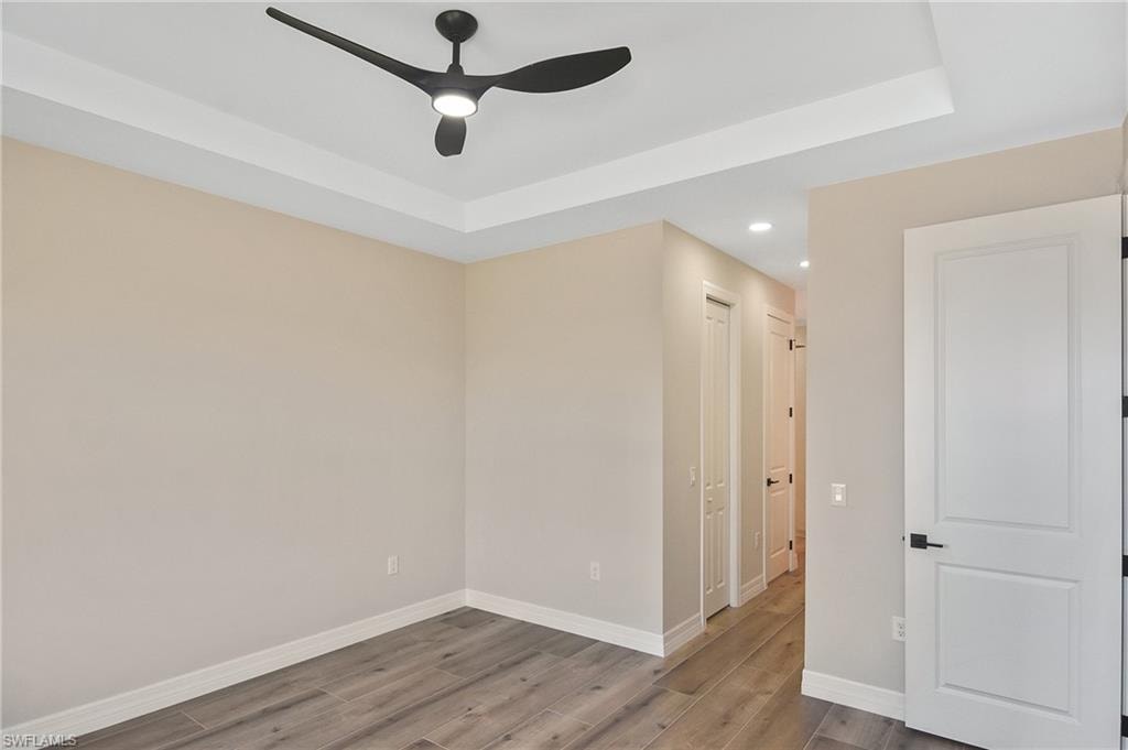 Tray ceiling with a modern ceiling fan, wood-finish flooring, recessed lighting, and white interior doors with black hardware