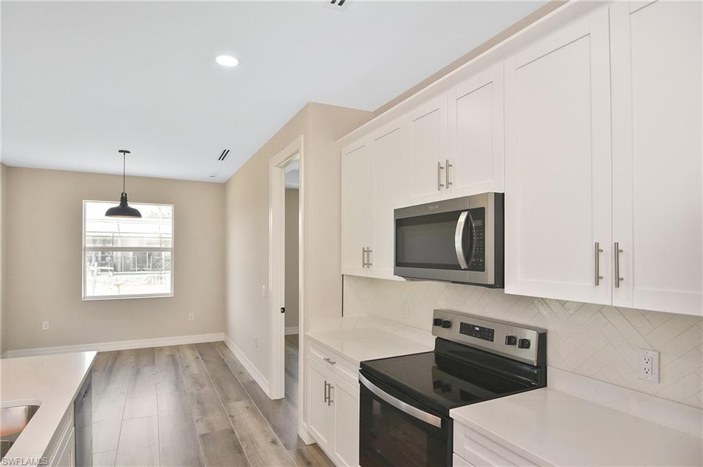 Contemporary kitchen featuring white shaker cabinetry, stainless steel appliances, light-toned countertops, and a subtle geometric pattern backsplash