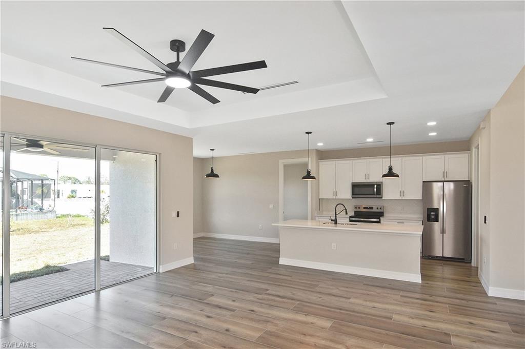 Open-concept living space featuring wood-finish flooring, a tray ceiling with a modern ceiling fan, and sliding glass doors providing access to the outdoor patio
