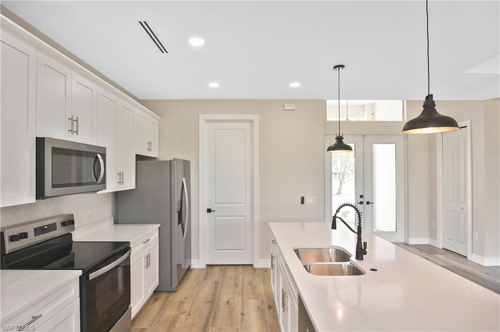 Modern kitchen featuring white cabinetry, stainless steel appliances, a large island with dual basin sink, and wood-finish flooring