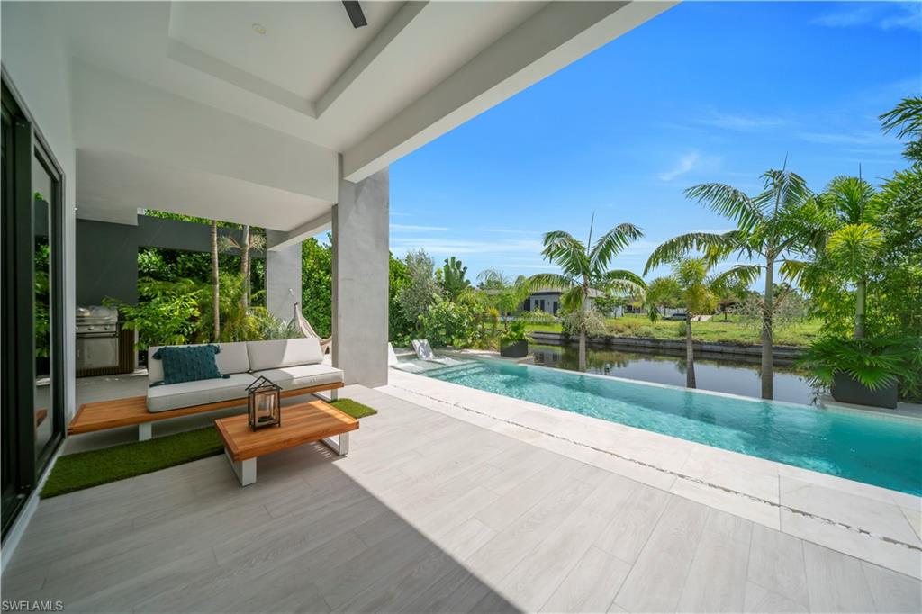 Covered patio with light-toned tile flooring, an outdoor kitchen, and an infinity-edge pool