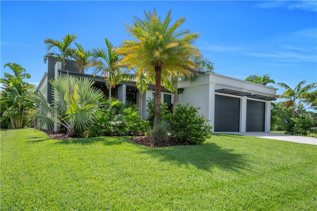 Contemporary exterior featuring a two-car garage with dark doors and awnings, a paved driveway, and a manicured lawn