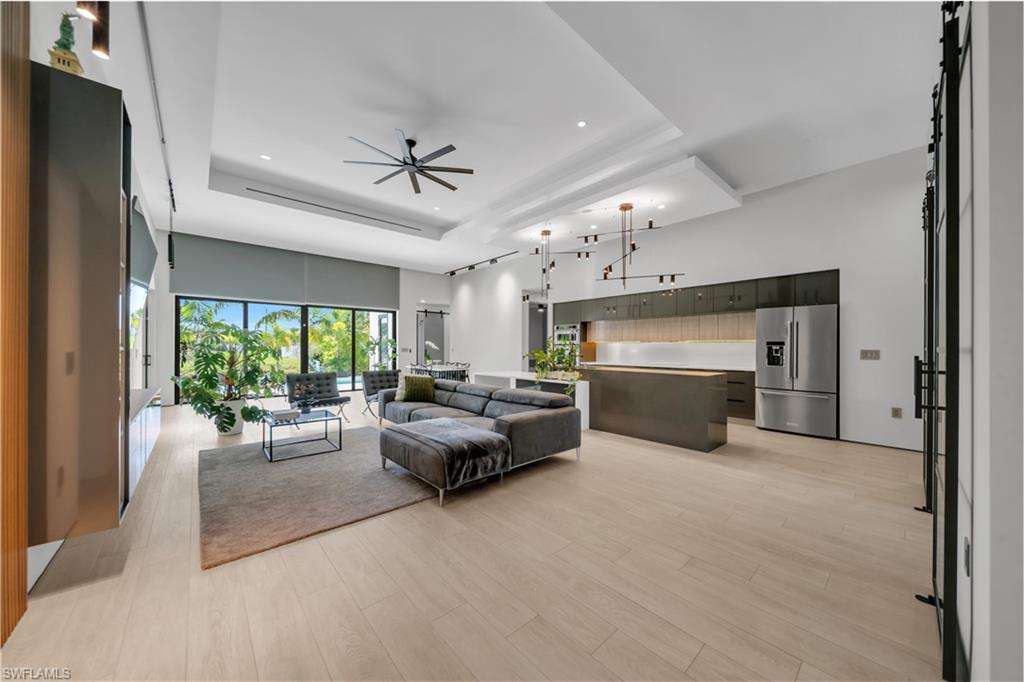 Expansive open-concept living space featuring light wood-finish flooring, a contemporary kitchen with stainless steel appliances, and a recessed ceiling with integrated lighting
