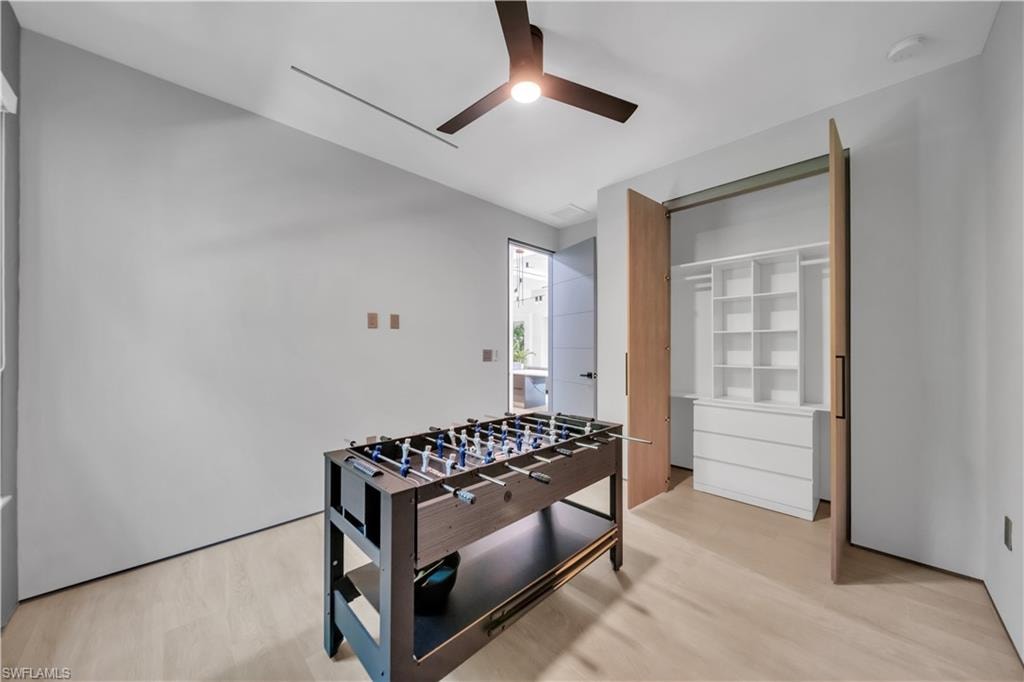 Room featuring light wood-finish flooring, a modern ceiling fan, and a built-in closet system with shelving and drawers