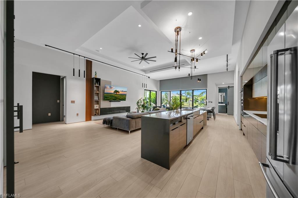 Open-concept living area with light wood-finish flooring, a contemporary kitchen island featuring an integrated dishwasher, and a living room with a linear fireplace
