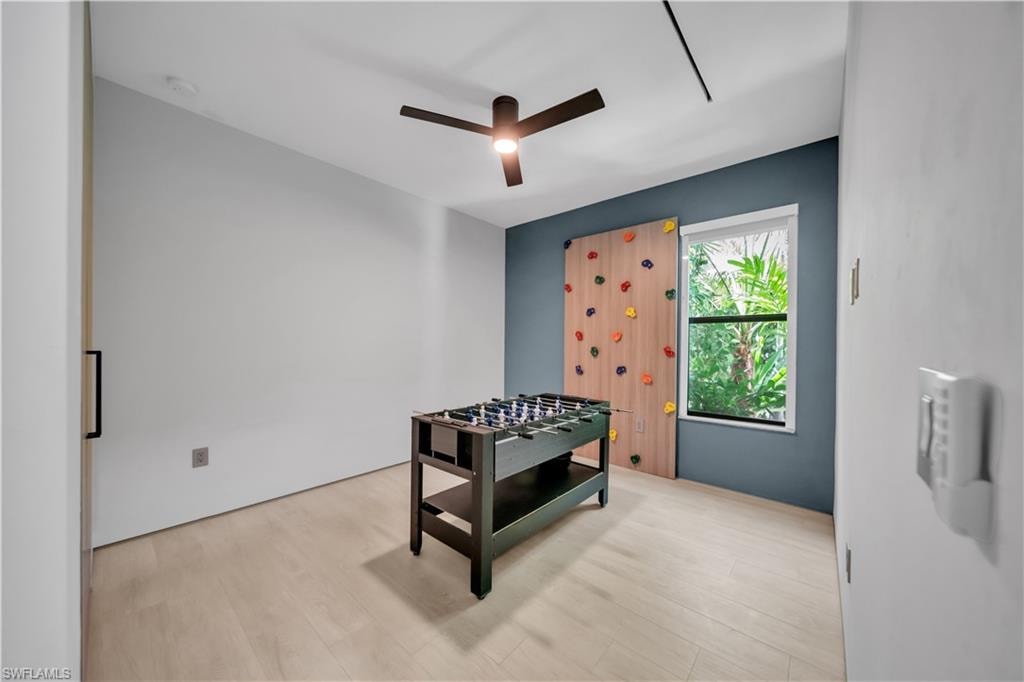 Bright room featuring light wood-finish flooring, a contemporary ceiling fan, and a bold accent wall with a built-in climbing panel