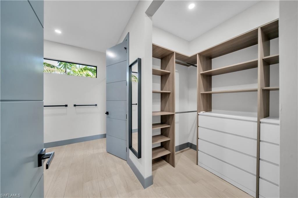 Spacious walk-in closet featuring extensive built-in shelving, integrated drawer storage, and wood-finish flooring
