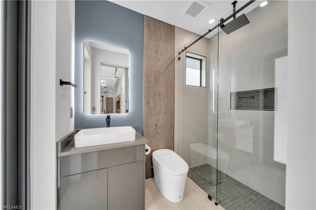 Bathroom featuring a floating vanity with a vessel sink, an illuminated mirror, and a wood-finish accent wall