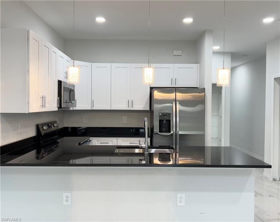 Contemporary kitchen featuring white cabinetry, dark countertops, stainless steel appliances, and pendant lighting