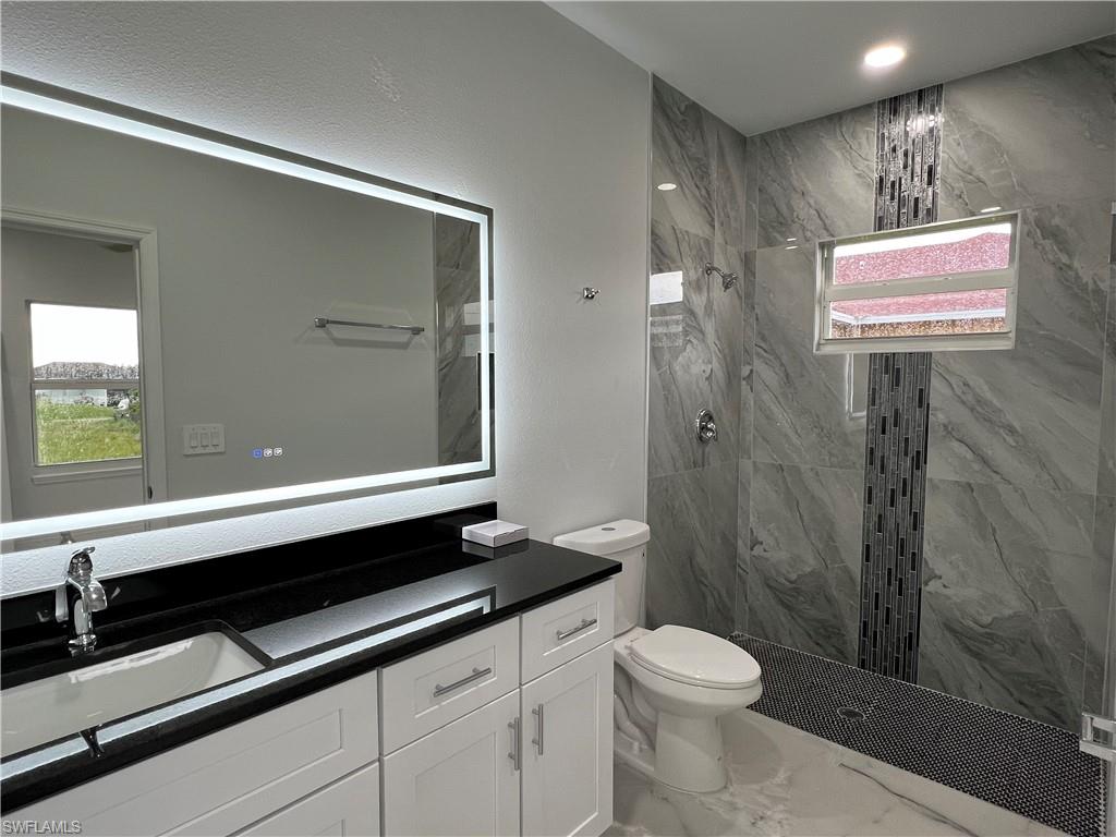 Bathroom featuring a lighted mirror, black countertop vanity with double-door cabinetry, and a walk-in shower with large-format tile and mosaic accents