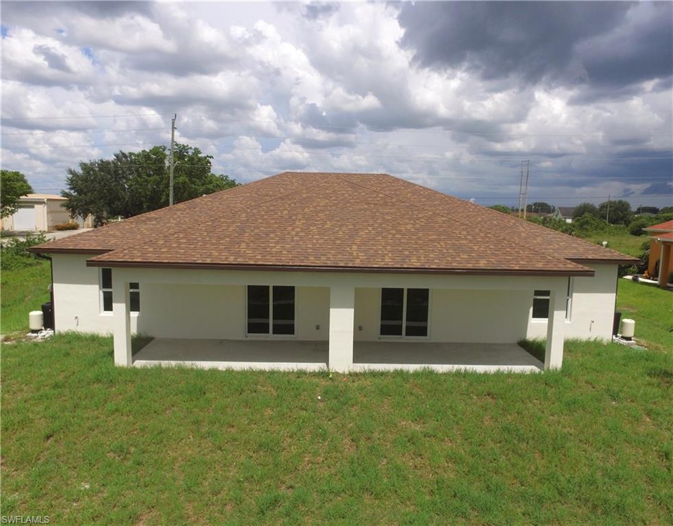 Rear exterior featuring a covered patio, multiple sliding glass doors, white stucco finish, and a brown shingle roof