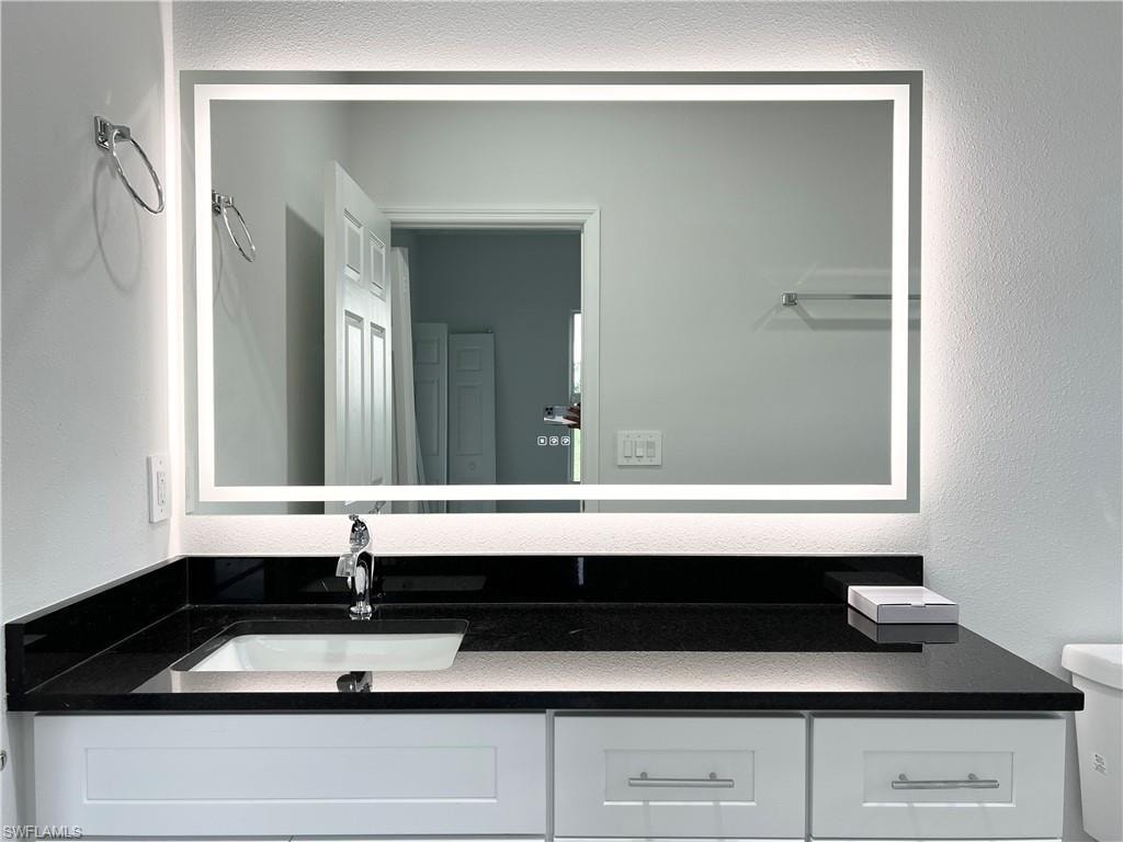 Vanity featuring a rectangular illuminated mirror, black countertop, undermount sink, and chrome faucet