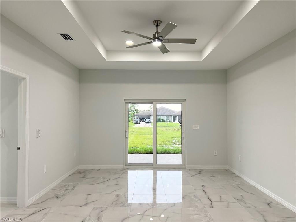 Spacious room featuring tray ceilings with a contemporary ceiling fan, large format marble-look tile flooring, and sliding glass doors opening to the backyard