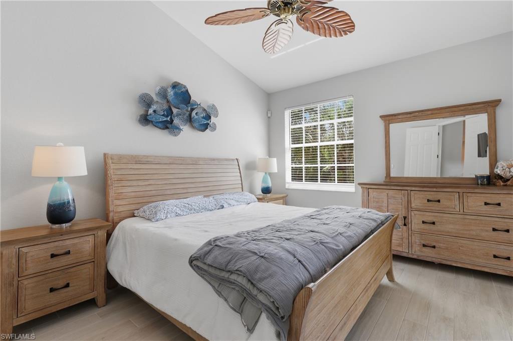 Vaulted ceiling bedroom featuring wood-finish flooring, a window with horizontal blinds, and a ceiling fan with palm leaf design blades