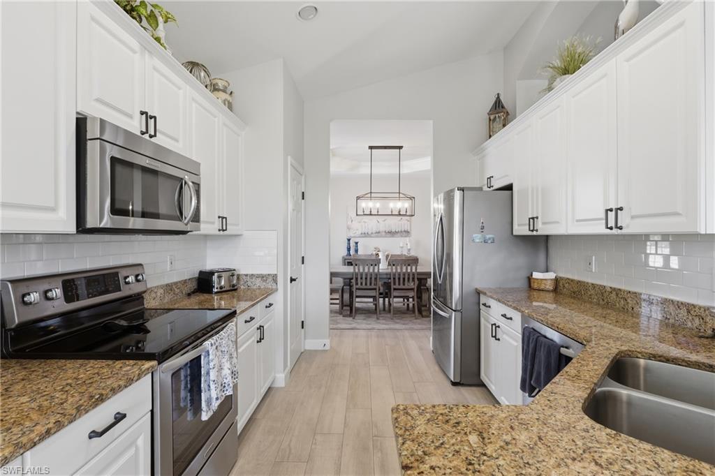 Galley kitchen featuring white cabinetry, stainless steel appliances, a double basin sink, light-toned wood-finish flooring, and speckled countertops