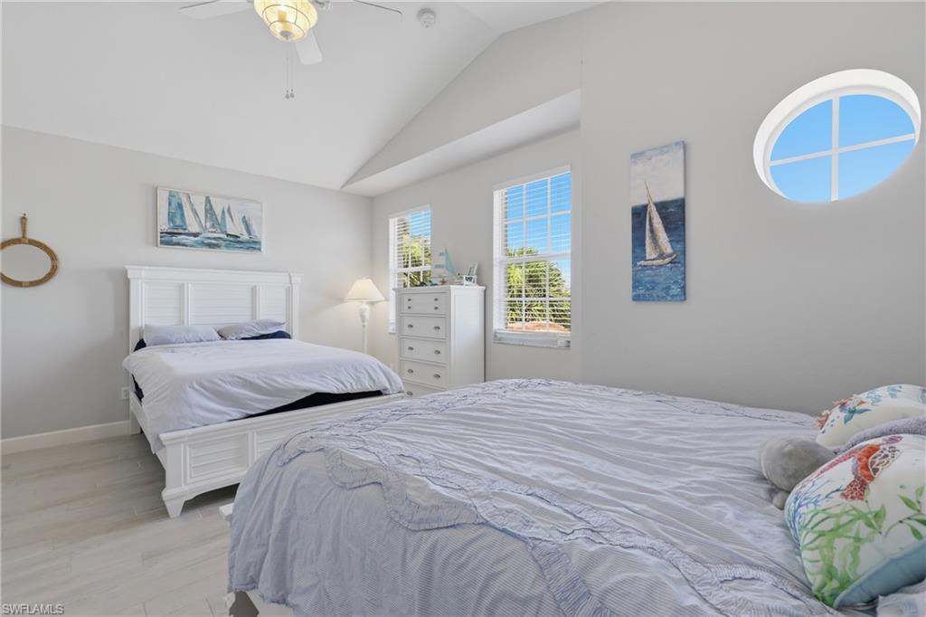 Vaulted ceiling room featuring light-toned wood-finish flooring, multiple windows including an oval-shaped window, and a ceiling fan with integrated lighting