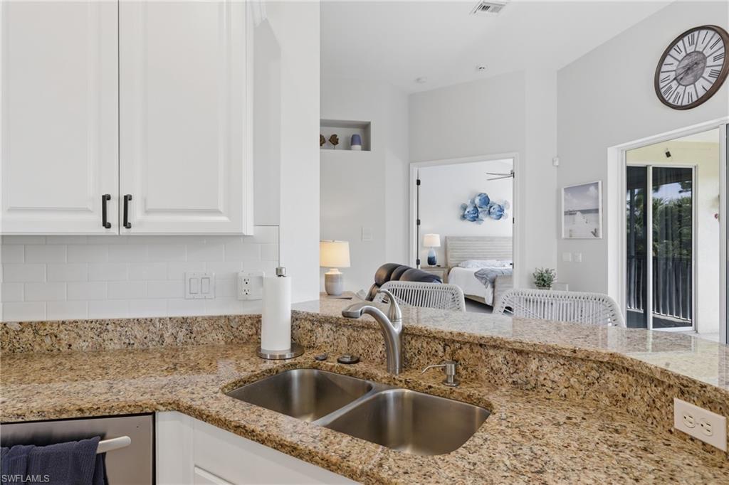 Kitchen featuring light-toned countertops, a double basin stainless steel sink with a gooseneck faucet, white shaker-style cabinetry with dark pulls, and a white subway tile backsplash