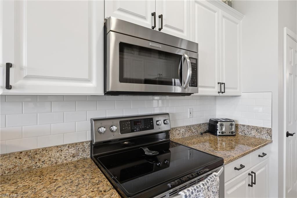 Kitchen featuring an electric range, stainless steel microwave, white shaker-style cabinetry with matte black hardware, and granite countertops