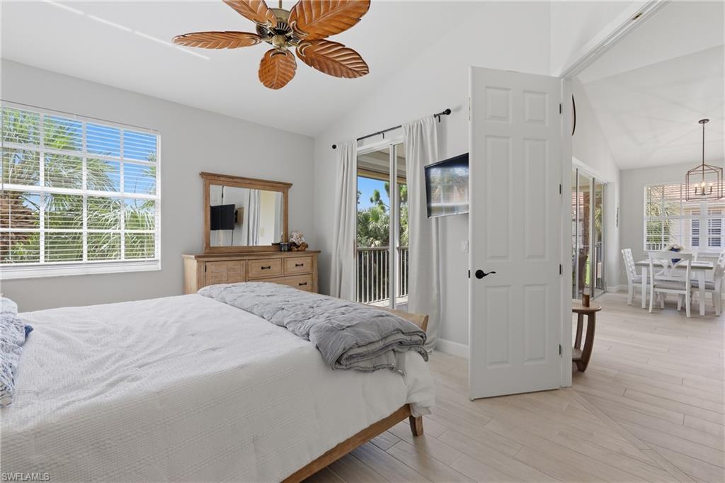 Vaulted ceilings with a decorative ceiling fan, large windows with horizontal blinds, wood-finish flooring, and direct access to an outdoor balcony