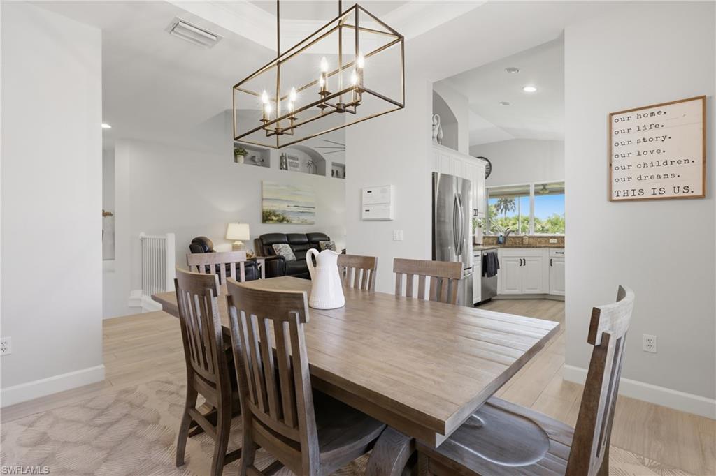 Dining area featuring a rectangular bronze-finish chandelier, vaulted ceilings, and light wood-finish flooring