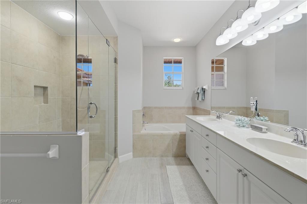 Spacious bathroom featuring a glass-enclosed shower with a built-in niche, a soaking tub with tile surround, a dual vanity with undermount sinks, and light wood-finish flooring