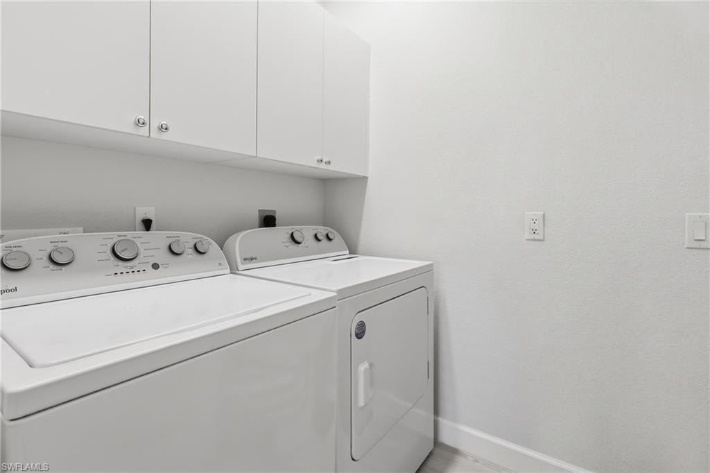 Laundry area featuring white cabinetry with silver-toned hardware, white appliances, and light-toned walls