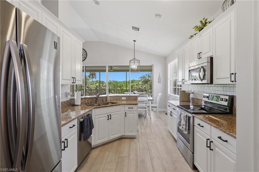 Modern kitchen featuring wood-finish flooring, white cabinetry with black hardware, stainless steel appliances, and light-toned countertops