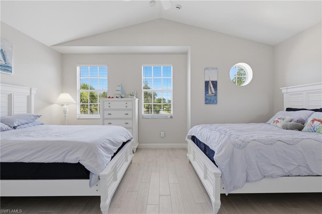 Bright bedroom featuring vaulted ceilings, light wood-finish flooring, two rectangular windows with blinds, and one circular window