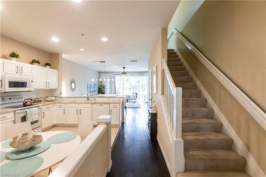Kitchen with white appliances, a peninsula, recessed lighting, white cabinets, and tasteful backsplash