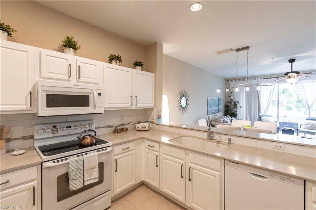 Kitchen with white appliances, light countertops, backsplash, ceiling fan, and light tile patterned flooring