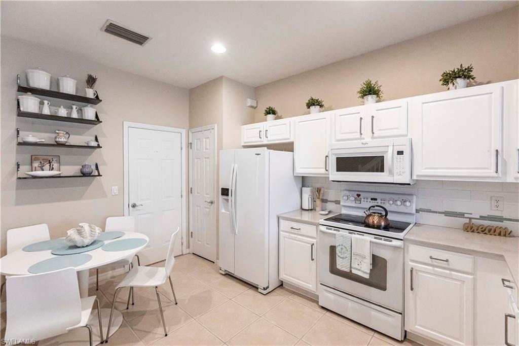 Kitchen featuring white appliances, white cabinetry, light countertops, backsplash, and light tile patterned floors