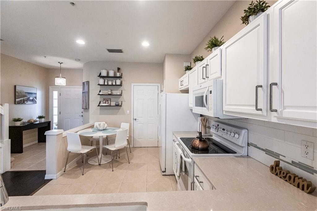 Kitchen with white appliances, light countertops, white cabinets, light tile patterned floors, and recessed lighting