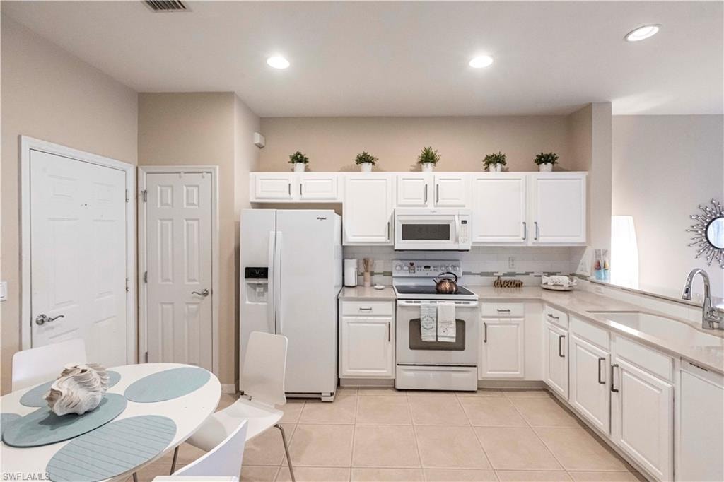 Kitchen with white appliances, light tile patterned floors, white cabinets, and recessed lighting