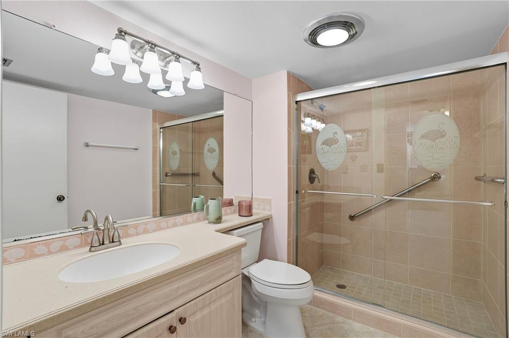 Full-length mirror spanning the vanity, single basin sink, light-toned countertop, vanity cabinetry with double doors, and a glass-enclosed shower with tiled walls