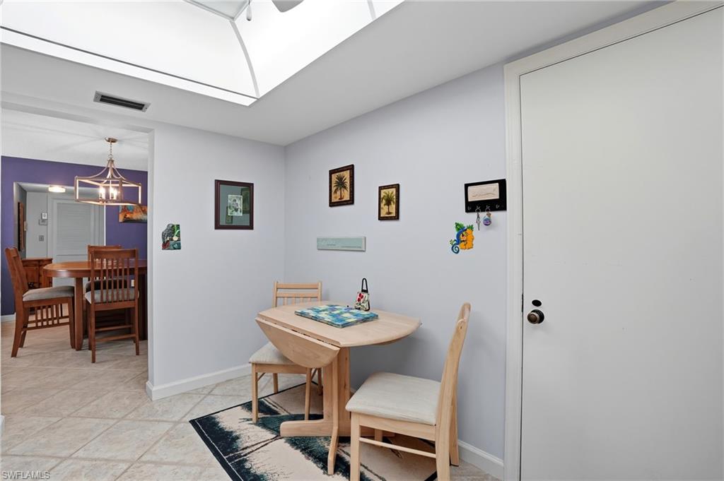 Recessed ceiling with an overhead skylight, tile flooring, and a dining area with a contemporary chandelier