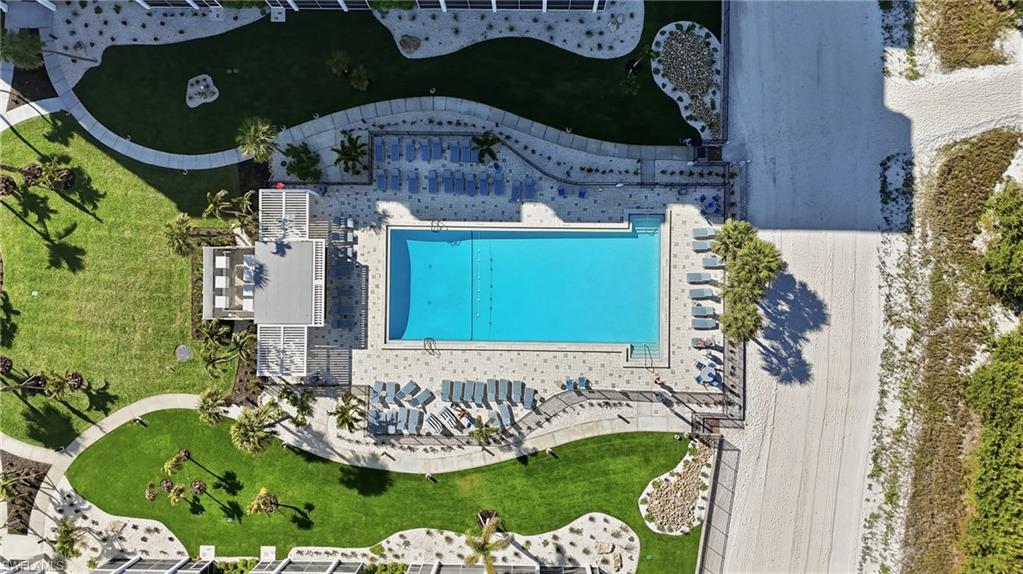 Rectangular swimming pool with a surrounding paver deck, multiple lounge chairs, and a shaded structure