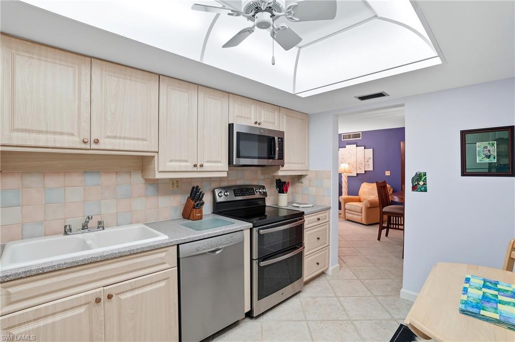Kitchen featuring wood-finish cabinetry, stainless steel appliances, a double basin sink, and tile flooring