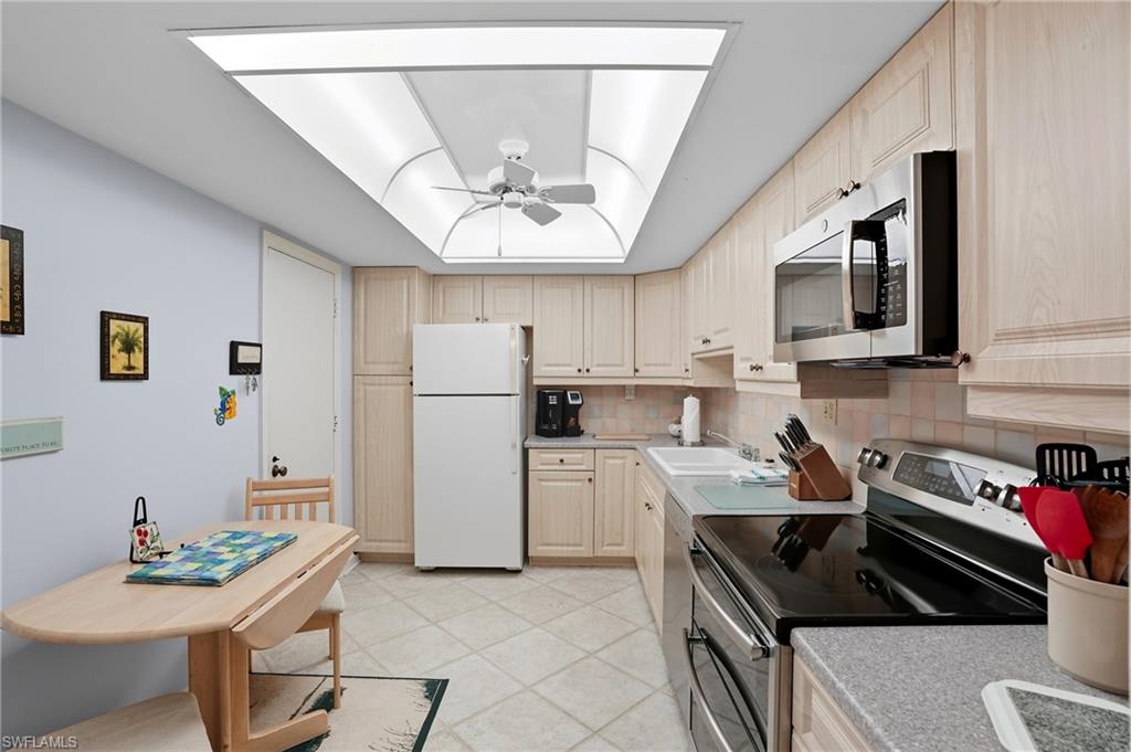 Kitchen featuring light wood-finish cabinetry, neutral tile flooring, and a luminous ceiling panel with a ceiling fan
