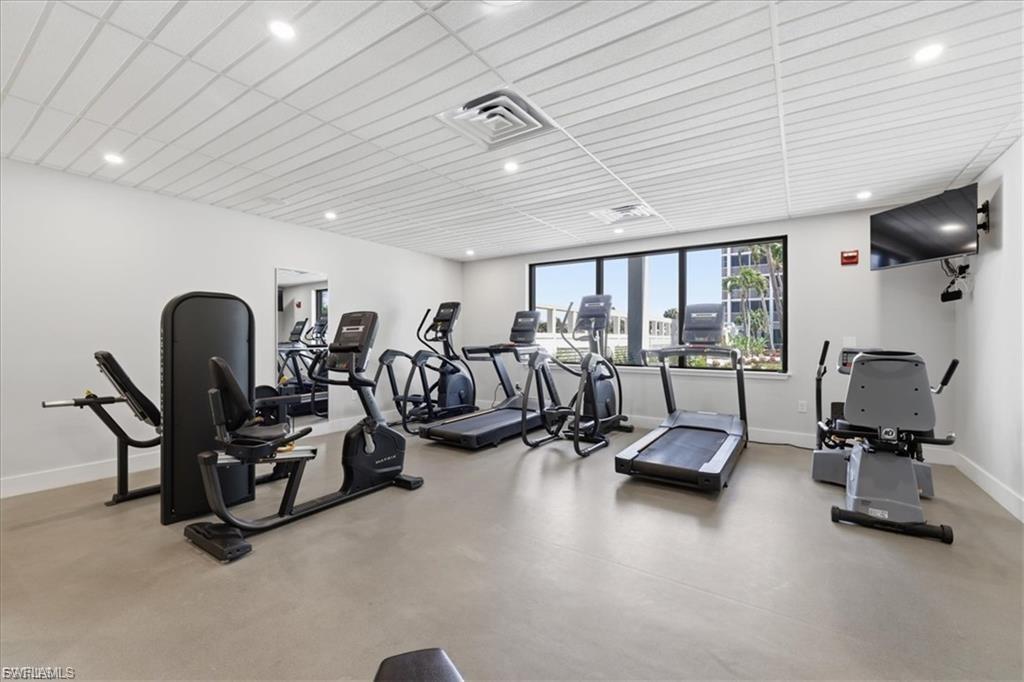 Fitness room featuring multiple exercise machines, large window with exterior scenery, wall-mounted television, recessed lighting, and a neutral flooring surface
