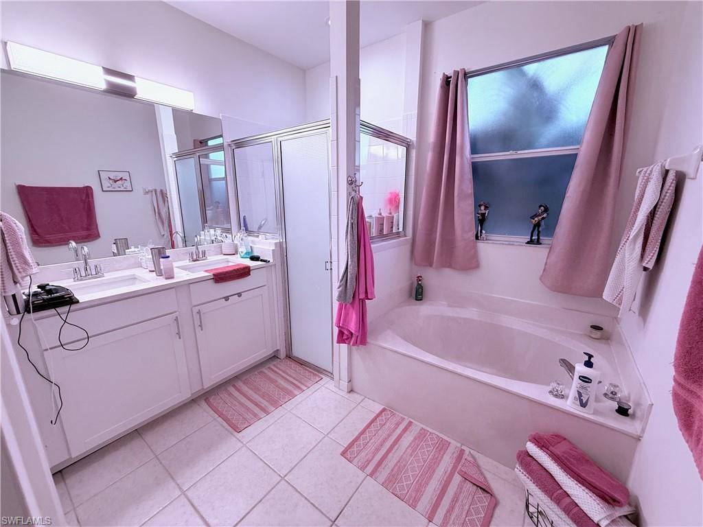 Dual vanity with integrated sinks, large mirrored wall, tile flooring, built-in soaking tub, and shower enclosure with framed glass