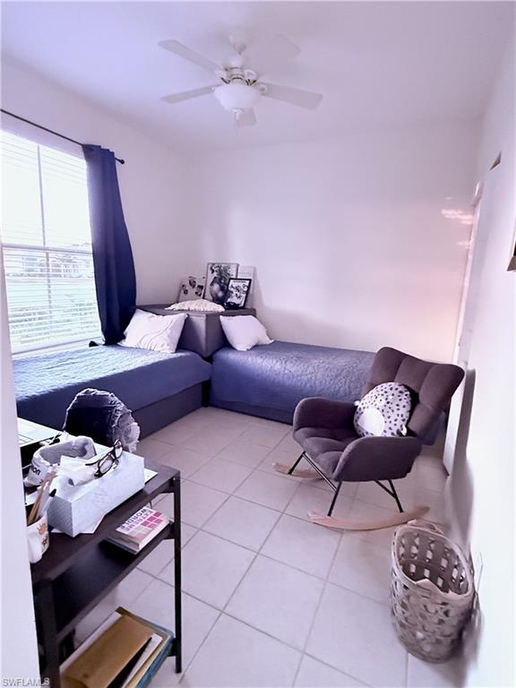 Recessed window with blinds, ceiling fan with light fixture, and light-toned tile flooring