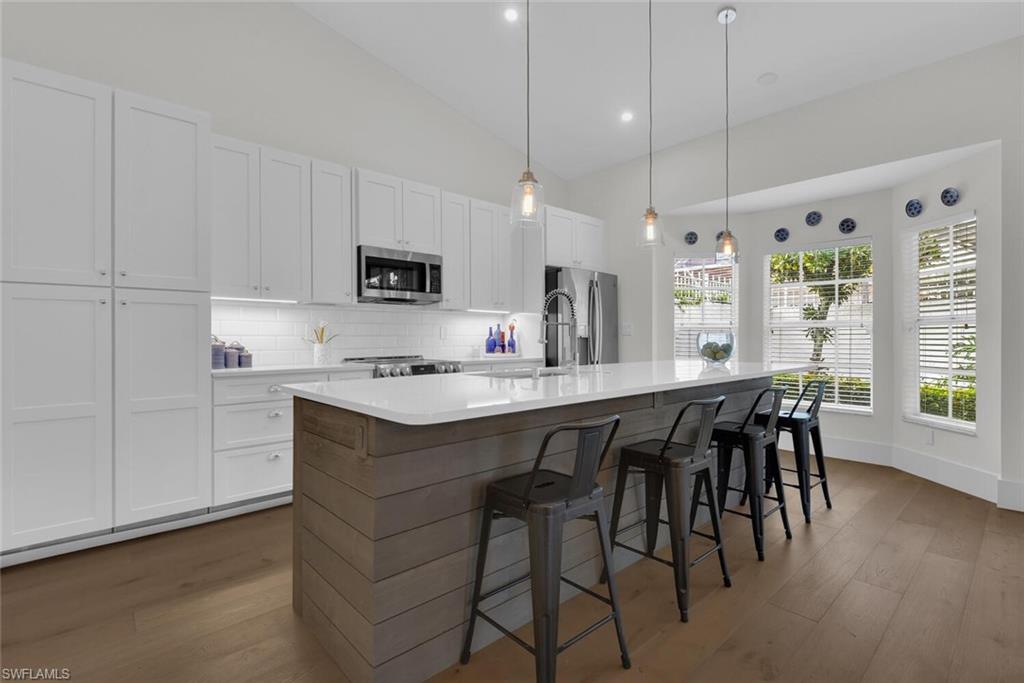 Kitchen with dark wood finished floors, tasteful backsplash, a center island with sink, white cabinetry, and high vaulted ceiling