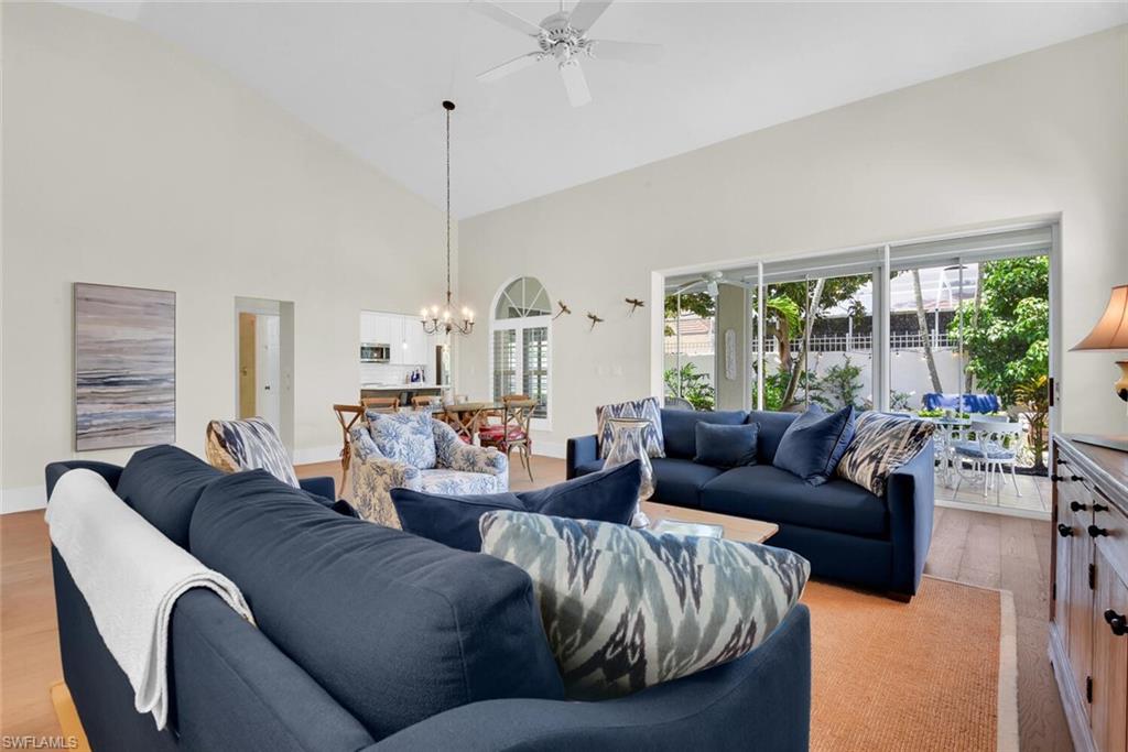 Living area with light wood-style floors, a ceiling fan, a chandelier, and high vaulted ceiling