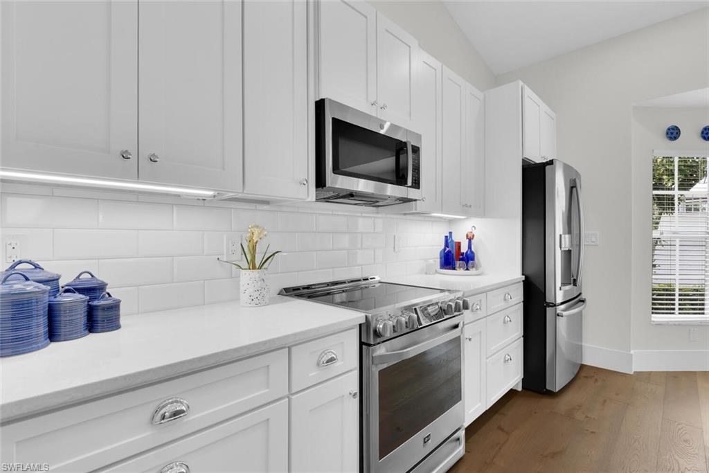 Kitchen featuring stainless steel appliances, dark wood finished floors, light countertops, and white cabinetry