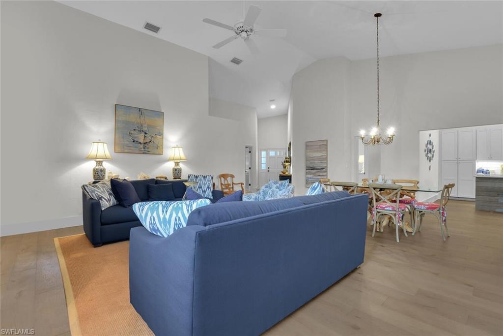 Living area featuring light wood finished floors, a chandelier, high vaulted ceiling, and a ceiling fan
