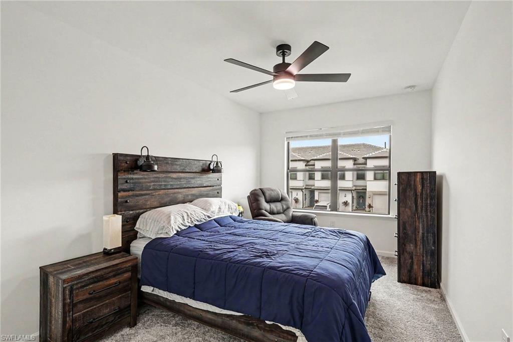 Bedroom featuring light grey carpeting, white painted walls, a large window, and a ceiling fan with integrated lighting