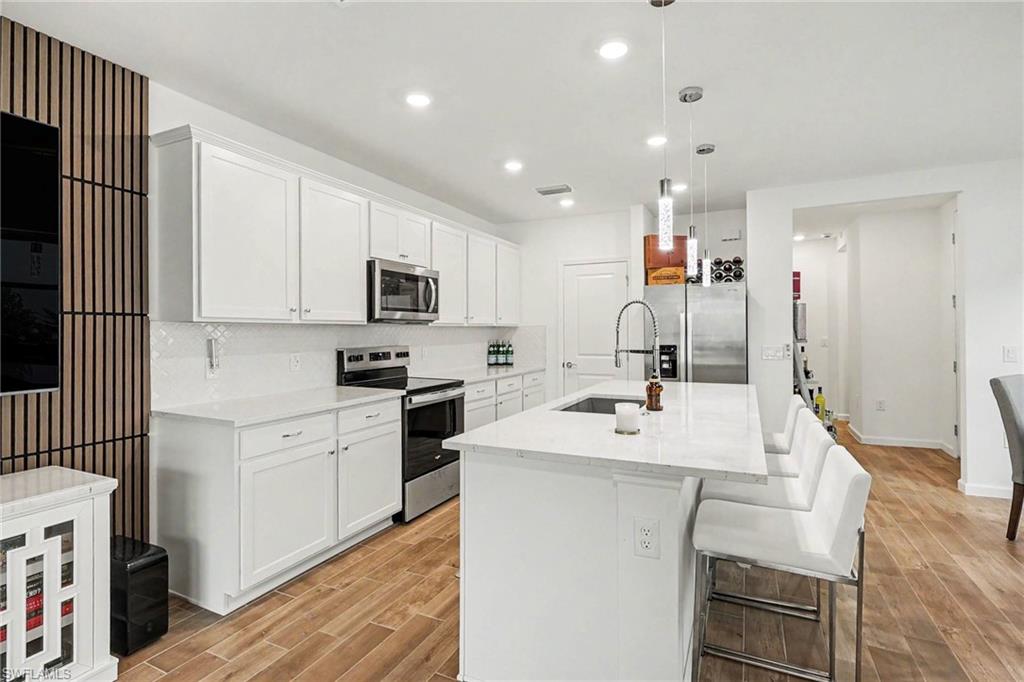 Contemporary kitchen featuring white cabinetry, a large center island with seating, stainless steel appliances, and wood-finish flooring