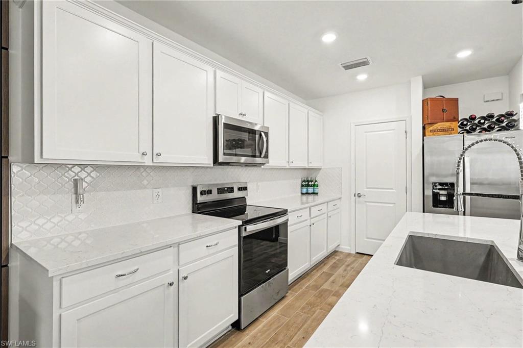 Modern kitchen featuring white shaker cabinetry, stainless steel appliances, a geometric tile backsplash, light-toned countertops, and wood-finish flooring